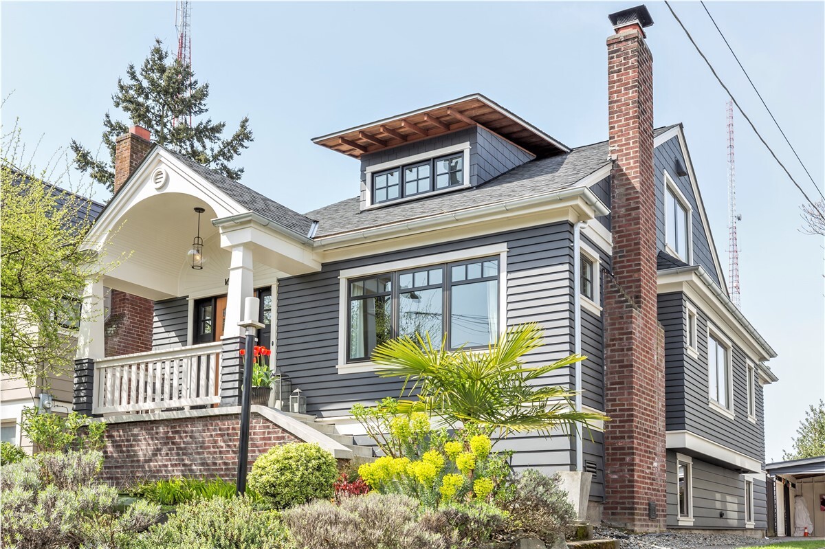 Craftsman home with gray siding, a brick chimney on a hill