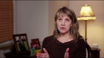 Woman talking with a lamp and picture frames in the background.