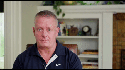 Man with black shirt sits in front of a white inset bookcase.