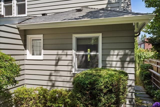 Light gray horizontal lap siding with a window facing inside with green bushes in front.