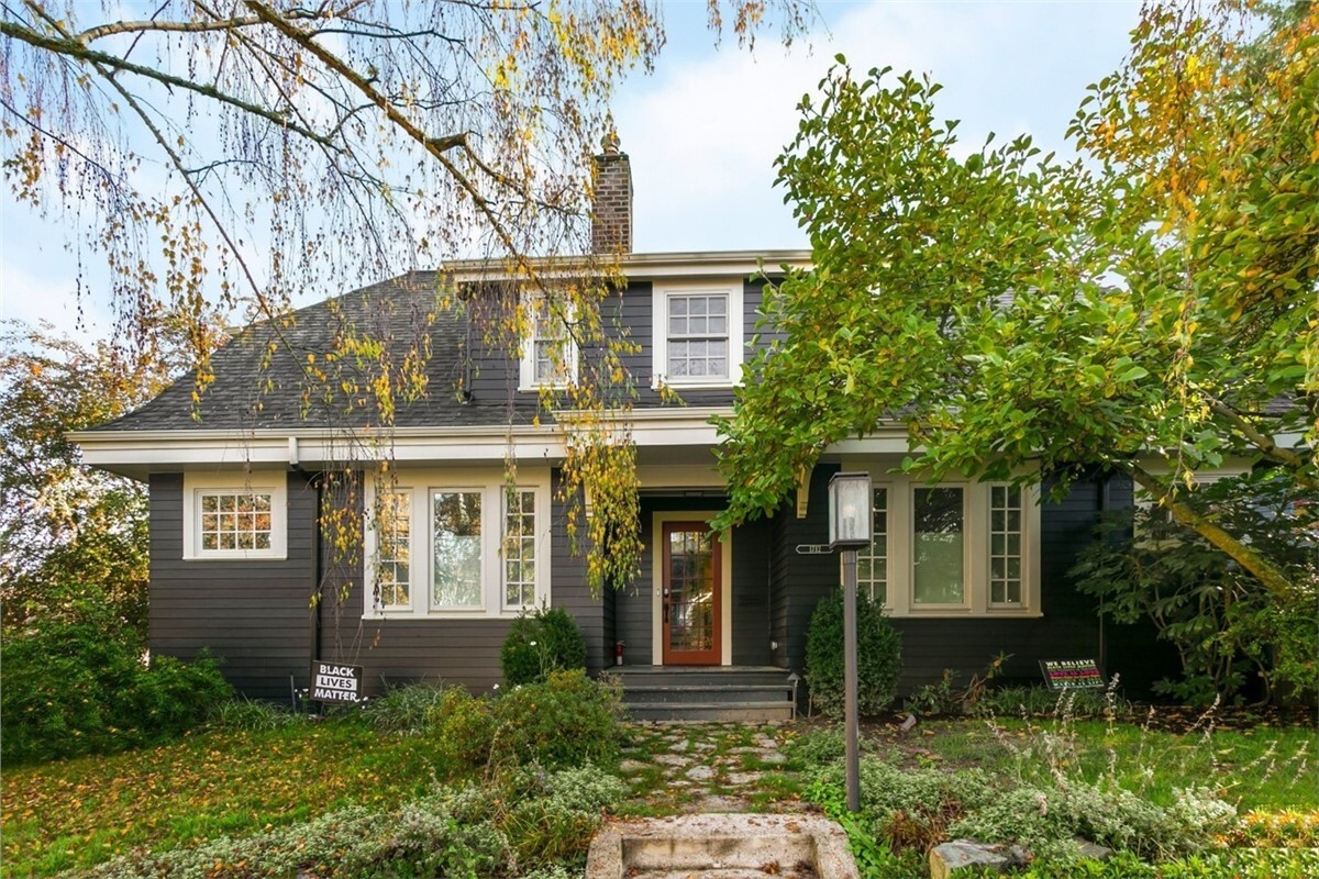 Dark gray siding with green garden and fall trees.